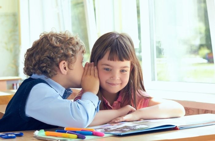 Child whispering into another child's ear 