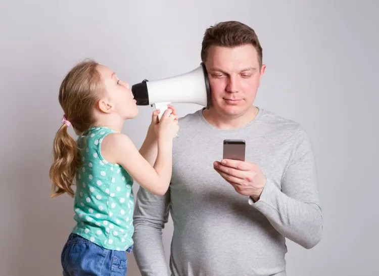 Child speaking into father's ear, who is on his phone, with loudspeaker