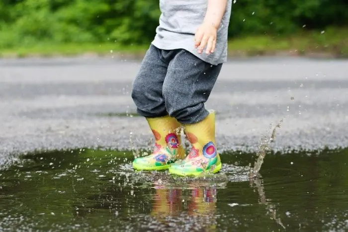 Messy play - boy splashing in wet puddles with boots on.