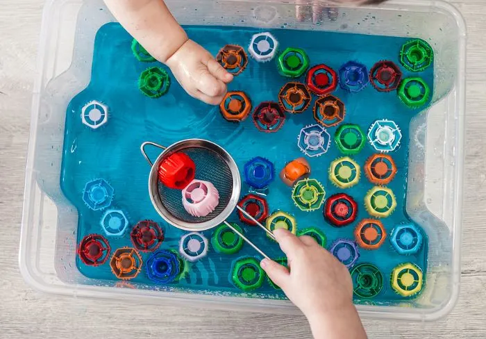 Messy play tray with bottle tops and water.