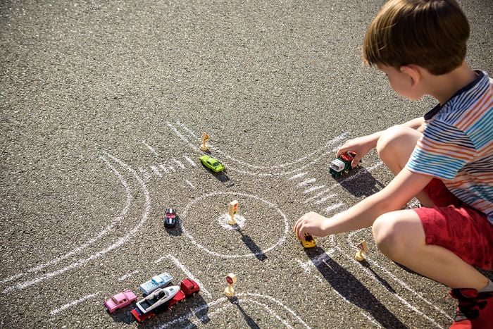 Child playing with cars on chalk-drawn track outdoors.