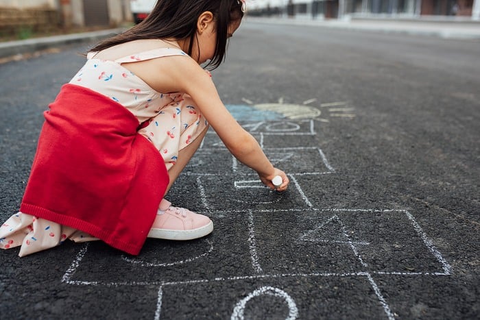 Little girl drawing with chalk to make hopscotch 