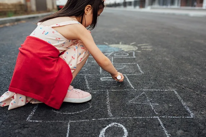 Little girl drawing with chalk to make hopscotch 