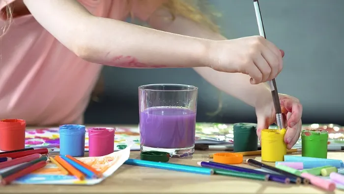 Child dipping paintbrush in paint pot.