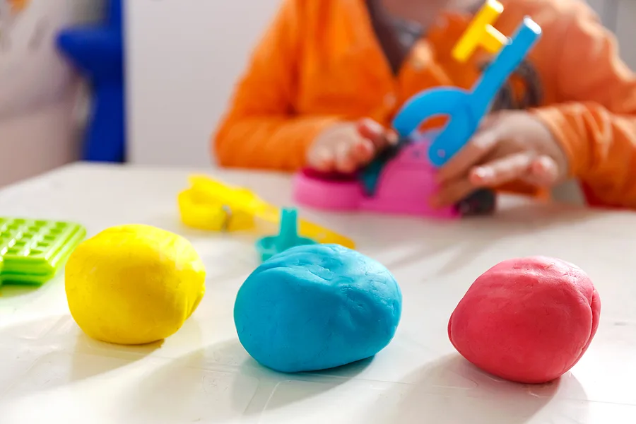 Three balls of playdough on table and child seated at table, playing.