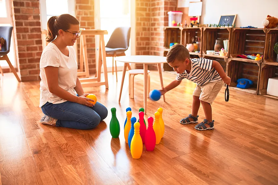 Toddler knocking plastic skittles over with a ball.