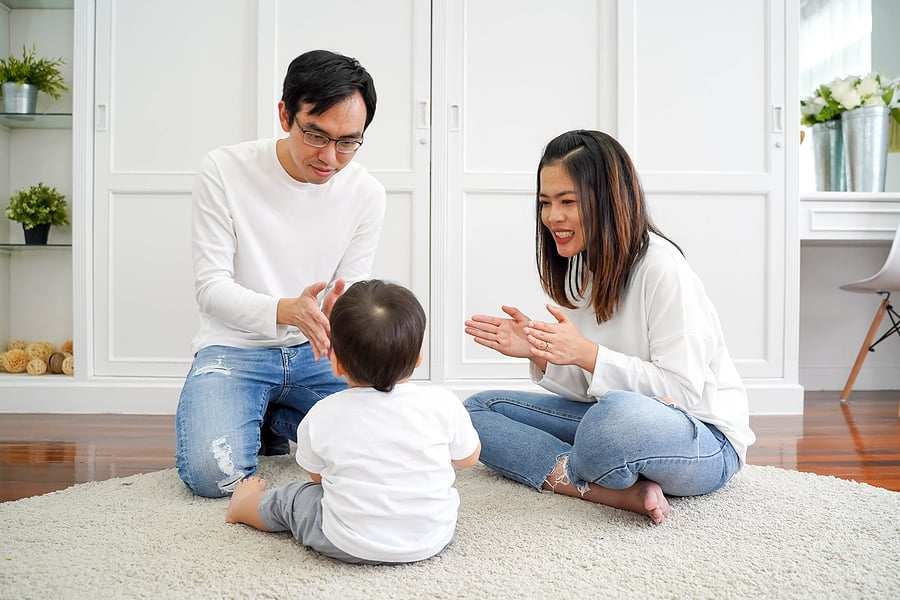 Parents seated on carpet with toddler and clapping hands together