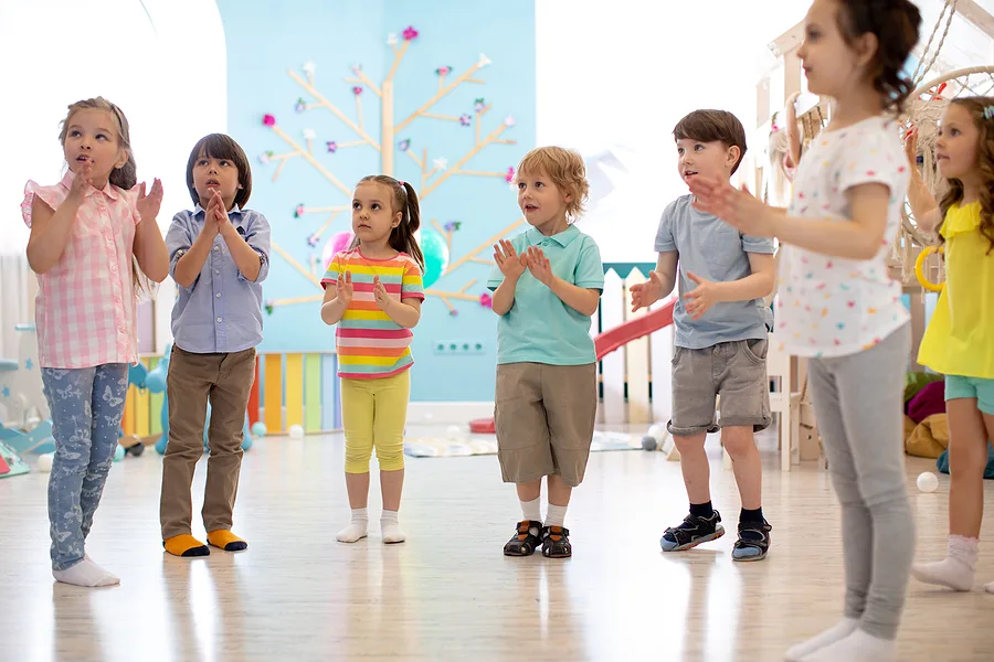 Preschoolers standing in a circle,  clapping hands to a song.