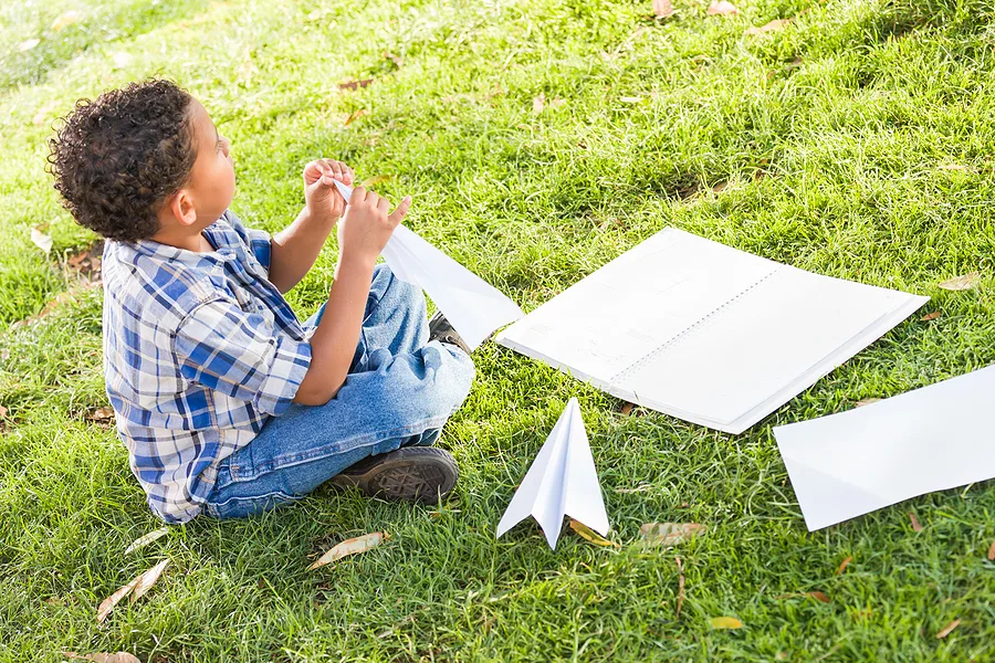 Child making paper airplanes on the grass
