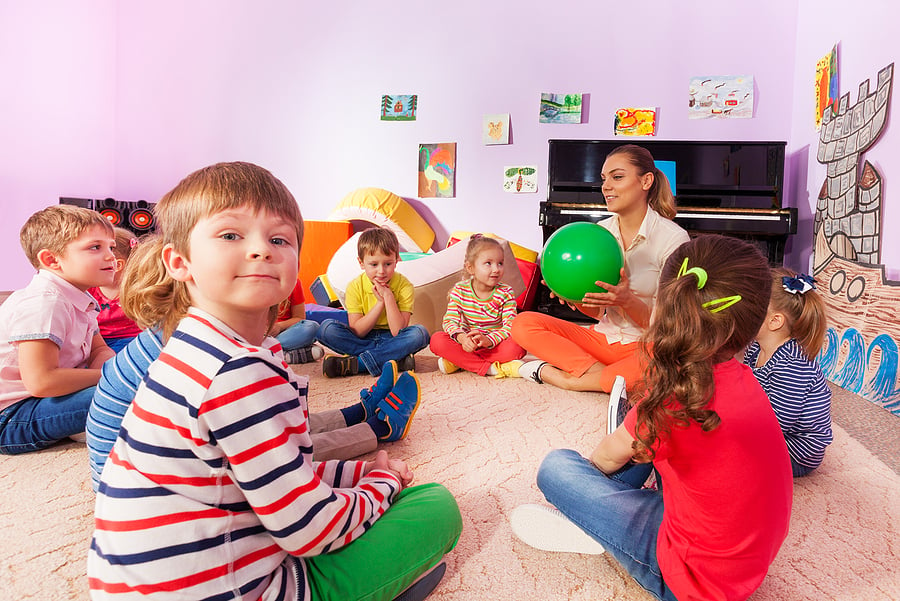 Children playing a carpet game with a ball in a classroom.