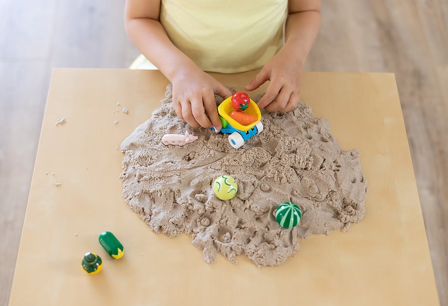 little child playing with kinetic sand and toys at table