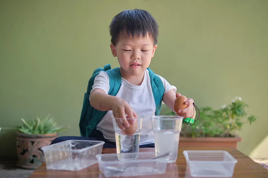 Little boy experimenting with eggs floating in water