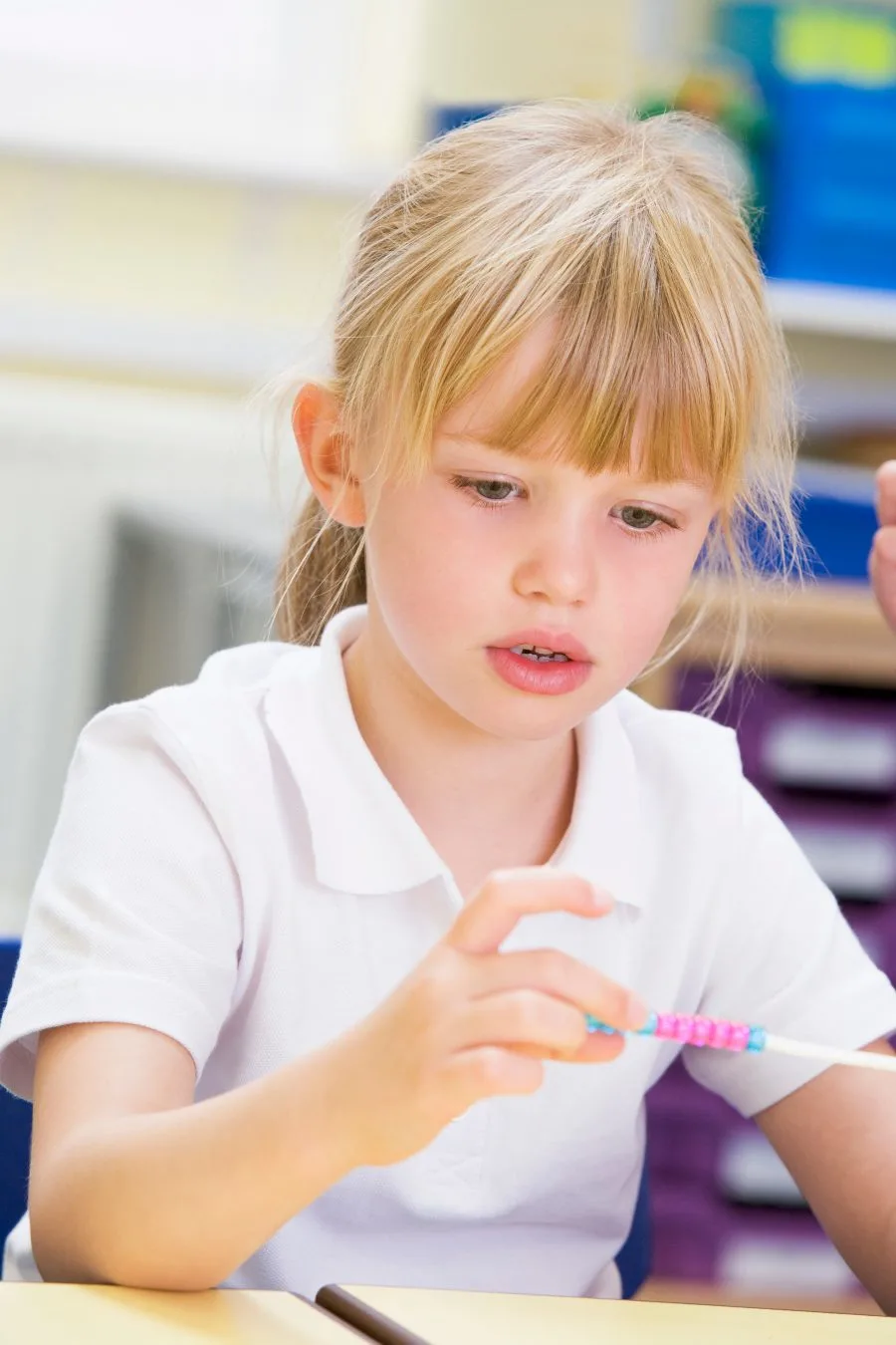 Kindergartener making a patterned beaded necklace