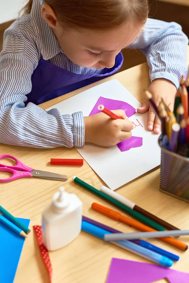 Little girl making a greeting card and writing on it