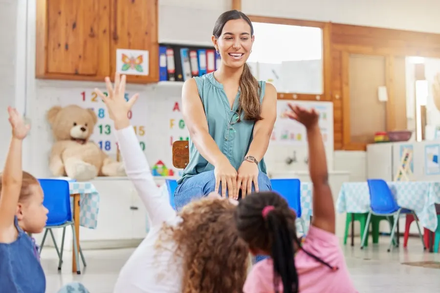 Preschoolers raising their hands to teacher in class