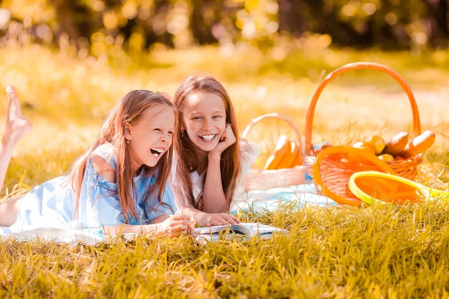 Two girls laughing together outside on a picnic blanket.