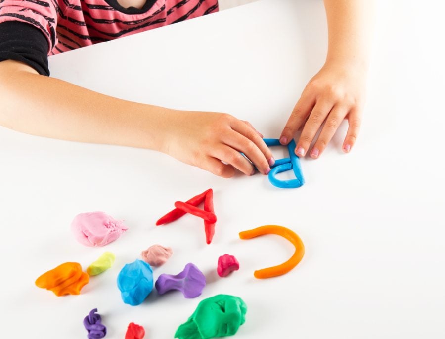 A child's hands shaping colorful playdough into letters