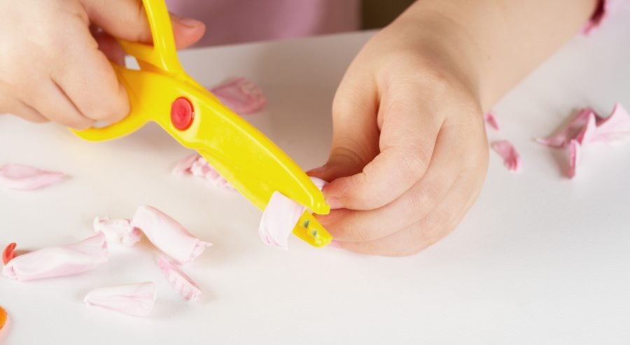 Child cutting up playdough with plastic scissors