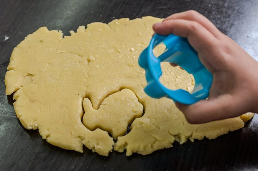 A child's hands pressing a cookie cutter into colorful playdough, creating a bunny shape
