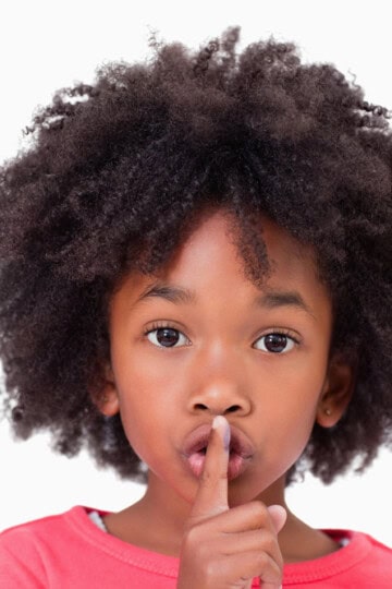 Young girl holding finger in front of mouth to show silence